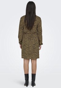Leopardenmuster-Kleid in Braun und Schwarz, mit langen Ärmeln, einem Gürtel in der Taille und knielangem Saum. Kombiniert mit schwarzen Stiefeletten.