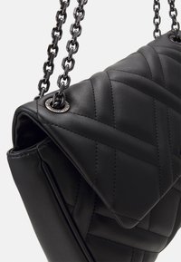 Borsa a tracolla in pelle nera trapuntata con catena, dotata di chiusura a pattina, hardware argentato e cuciture diagonali per un effetto texture.