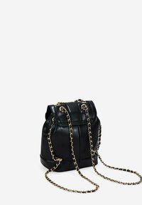 Mochila de cuero negro con correas de cadena doradas, parte superior ajustada y detalles de costura vertical en el frente. Diseño compacto y estructurado.