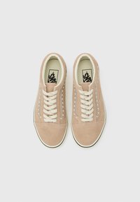 Paire de baskets Vans en daim beige avec des lacets blancs et la bande latérale emblématique, vues de dessus sur un fond uni.