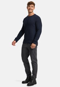 Pullover navy in maglia con texture a coste, scollo tondo e maniche lunghe, abbinato a jeans grigio scuro e stivali neri con lacci.