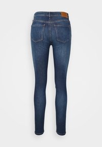 Jeans ajustados de mezclilla azul oscuro. Cuenta con una cintura de altura media, dos bolsillos traseros y una etiqueta de cuero en la parte trasera con el logo de la marca.