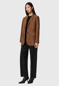 Bruine suède blazer met inkepingen, enkel geborduurd ontwerp, twee voorkruiszakken, gecombineerd met zwarte wijdvallende jeans en puntige hakken.