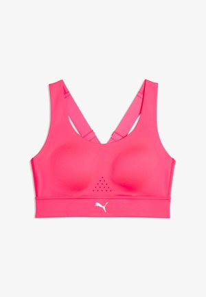 Brassière de sport rose vif avec bretelles croisées dans le dos et petits trous de ventilation sous la poitrine, ornée d'un logo Puma blanc sur la bande.