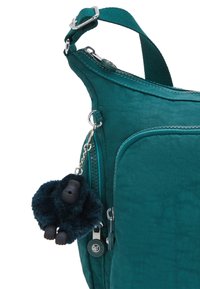 Teal fabric shoulder bag with a textured finish, featuring a zippered pocket and a plush gorilla keychain accessory attached.