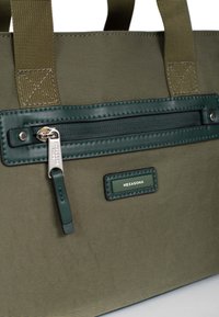 Borsa tote verde oliva con tessuto testurizzato, caratterizzata da una tasca centrale con zip, dettagli in pelle verde e un'etichetta con logo. Cuciture rinforzate sul manico.