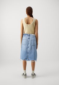 Top de punto beige con bordes festoneados, combinado con una falda de mezclilla azul clara con dobladillo sin terminar y bolsillos traseros. Zapatillas grises con suelas blancas.