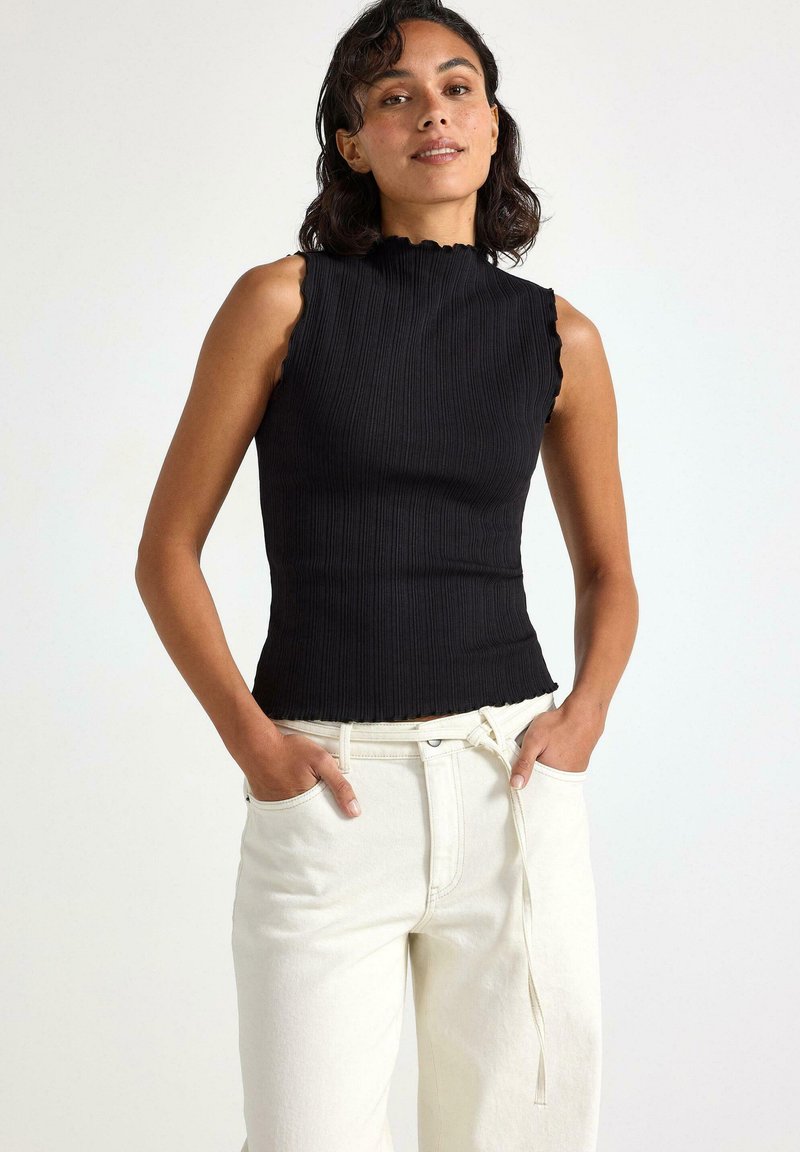 Sort ribbet tanktop med en bølgede halsudskæring, parret med hvide vidde bukser. Toppen har et tætsiddende design og struktureret stof.