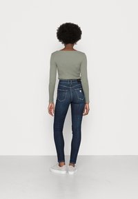 Mörkblå skinny jeans i denim, med bakfickor som har en triangulär logodetalj. Matchas med en åtsittande ljusgrön ribbad topp.