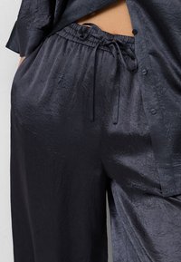 Dunkelblaues Zweiteiler-Outfit bestehend aus einem locker sitzenden Hemd mit Knöpfen und elastischen Bundhosen, gefertigt aus glattem, strukturiertem Stoff.