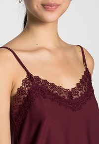 Bordeaux camisole met dunne bandjes, met een delicaate kantafwerking langs de halslijn. Smooth stof met een zachte textuur, minimalistisch ontwerp.