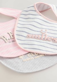 Trois bavoirs de couleurs variées : un rose avec une texture côtelée, un blanc avec des rayures navy, et un gris avec des lettres douces. Chacun présente un texte distinct.