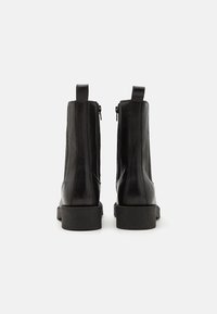 Bottines en cuir noir avec une texture lisse, fermeture éclair et semelle à plateforme basse. Équipées d'une languette pour un enfilage facile.