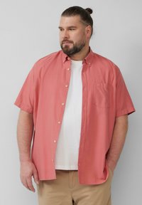 Korte mouw, koraalkleurige overhemd met knopen en een enkel borstzakje, gedragen over een wit T-shirt, gecombineerd met beige broek. Glad stofgevoel.