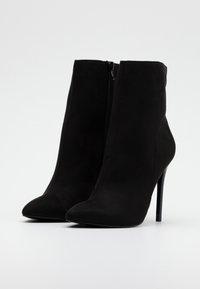 Botas de tobillo negras de ante con punta afilada y cremallera lateral. Presentan un tacón delgado y alto para un estilo elevado.