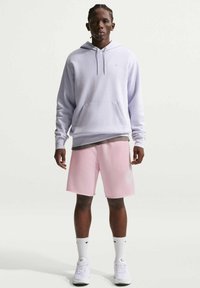 Vaaleanlaventelin värinen huppari etutaskulla; yhdistetty vaaleanpunaisten shortsien kanssa, joissa on hillitty logo, ja valkoiset tennarit.