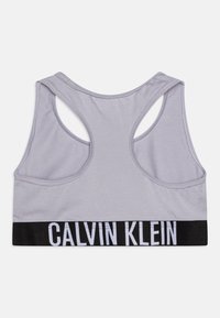 Siva športna srajca, ki ima obliko racerback, mehko tkanino in črn elastični pas z belim logotipom "CALVIN KLEIN" na dnu.