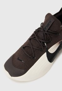 Schwarze Nike-Sneaker mit einer strukturierten Oberseite, ausgestattet mit einer dicken Creme-Sohle und schwarzen Akzenten, darunter ein markantes Logo an der Seite.