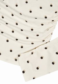 Roomkleurige stof met een gerimpeld ontwerp, voorzien van verspreide stippen in zwart en beige. Zachte textuur met een aansluitende mouw.