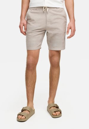 Beige linen shorts with a drawstring waistband, side pockets, and a relaxed fit, paired with brown two-strap sandals.