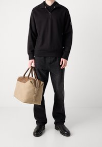 Svart zip-up sweatshirt med en texturerad yta, parat med svarta jeans och svarta skor. Håller en beige och brun läderväska med dragkedjor.