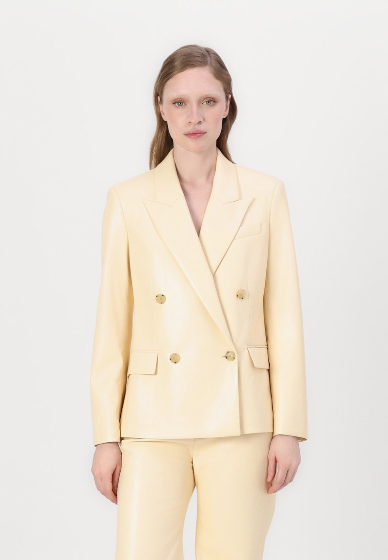 Blazer doppiopetto in pelle lucida di un giallo chiaro. Presenta bottoni dorati, rever affilati e due tasche frontali. Vestibilità sartoriale.