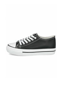 Deportivas negras de caña baja con suela de goma blanca, puntera blanca, cordones blancos y costuras blancas sobre un fondo liso.