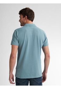 Camisa polo de color azul claro con mangas cortas y cuello con solapa, hecha de tela suave, mostrada desde la parte de atrás con un diseño liso.