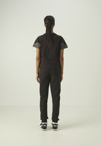 Top atletico nero con accenti grigi, vestibilità rilassata. Abbinato a pantaloni neri affusolati e scarpe nere. Design minimalista con tessuto testurizzato.