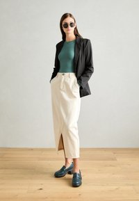 Černý blazer, těsný top v barvě mořské zeleně, krémová sukně s předním rozparkem a tmavě tyrkysové dřeváky. Hladké textury s moderním designem.