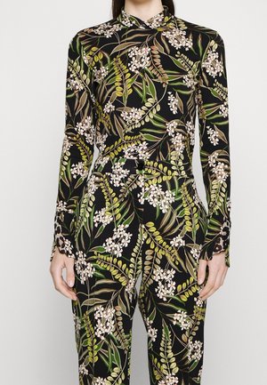 Frau trägt ein passendes langärmeliges Shirt und Hose mit schwarzem Hintergrund und grünem, braunem und weißem Blumen- und Blattmuster.