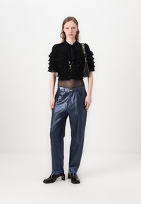 Top nero corto con strati di volants, bottoni decorati e cravatta; pantaloni blu lucidi a vestibilità ampia; stivali neri con tacco; borsetta piccola.
