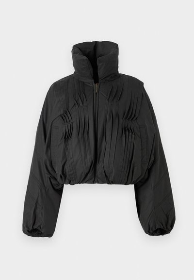 Giacca nera corta con pieghe verticali, colletto alto e chiusura con zip. Presenta maniche ampie con polsini elasticizzati. Tessuto liscio e leggero.