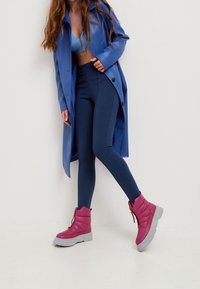 Abrigo de vinilo azul, top azul claro, leggings azul marino y botas de tobillo acolchadas rosas con suelas grises, que cuentan con cierre de cremallera y diseño acolchado.