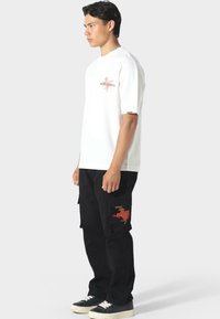 Camiseta de algodón blanca de manga corta con un diseño gráfico rojo en el pecho. Pantalones cargo negros con bolsillos laterales y acentos rojos.