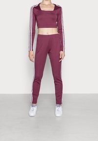 Set sportivo bordeaux con top cropped a maniche lunghe e pantaloni affusolati. Strisce bianche ai lati e dettagli con logo su entrambi i pezzi. Tessuto testurizzato.