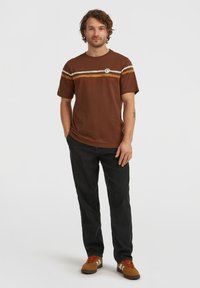 Brown cotton t-shirt featuring horizontal stripes in cream and orange. Paired with black jeans and brown sneakers with red accents.