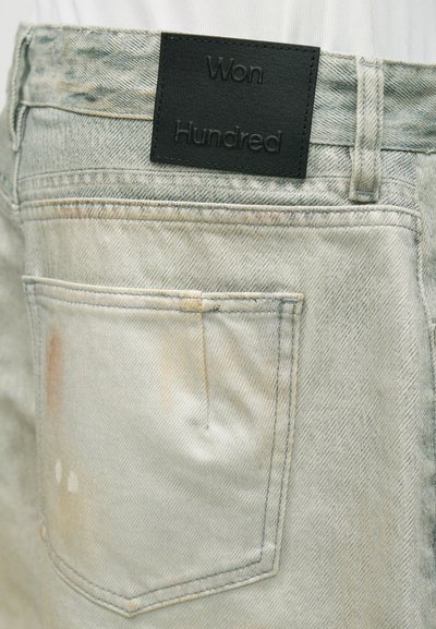 Πίσω τσέπη από τζιν φθορίου με ξεθώριασμα και μια μαύρη ορθογώνια ετικέτα πάνω της με ανάγλυφη την επιγραφή «Won Hundred.»