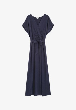 Donna che indossa un abito lungo blu navy a maniche corte con cintura e scarpe con tacchi alti nere, di spalle su uno sfondo semplice.