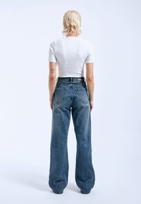 Hoge taille, wijde blauwe denim jeans met een vervaagde wassing en vijf zakken. Gecombineerd met een aansluitend wit katoenen t-shirt.