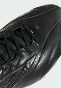 Κοντινή λήψη μαύρου αθλητικού παπουτσιού με υφή στη σόλα, μαύρα κορδόνια και διακριτική σήμανση στο πλάι.