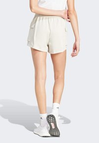 Beige cargo šortky s elastickým pasem, se dvěma bočními kapsami a texturovanou tkaninou. Stylizované s bílými sportovními botami a ponožkami.