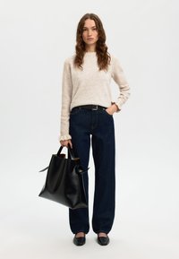 Gaiši bēšs džemperis ar garām piedurknēm, tumši zili plata piegriezuma džinsi un liela melna ādas soma ar divām rokturiem. Melni dzīvokļveida apavi.