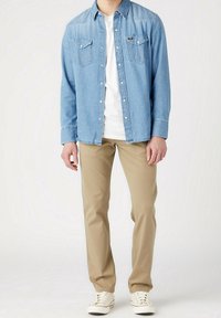 Lichtblauwe denimhemel met twee borstzakken, gecombineerd met beige broeken en witte sneakers. De hem heeft knoopsluitingen en een klassieke kraag.