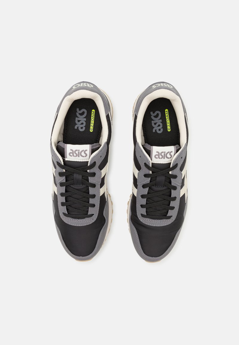 Chaussures de sport noires et grises avec trois rayures blanches, un fini texturé, un design à lacets et une semelle intérieure rembourrée étiquetée "EZ-FOAM."