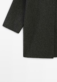 Tmavě šedá vlněná rukáv a dolní část na bílém pozadí, ukazující chlupatou texturu a rovné střižené okraje.