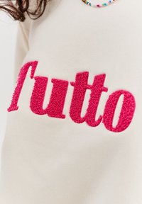Krémová bavlněná mikina se snagými růžovými nápisy "Tutto" s výrazně zobrazenými tučnými, měkkými, texturovanými písmeny.