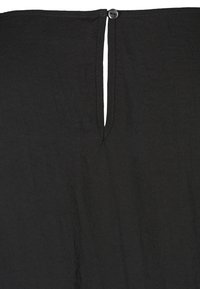 Musta kangas, jossa pieni yksittäinen nappi sulkemassa yläreunan lähellä olevaa kapeaa pystysuuntaista aukkoa.