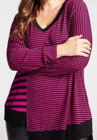 Långärmad topp med rosa och svarta ränder, V-krage och kontrasterande helt svart fåll. Mjukt tyg med avslappnad passform och strukturerat mönster.