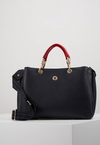 Czarna skórzana torebka z kontrastującymi czerwonymi uchwytami, złotymi detalami i odpinanym niebieskim paskiem w paski. Logo na froncie. Gładka faktura.